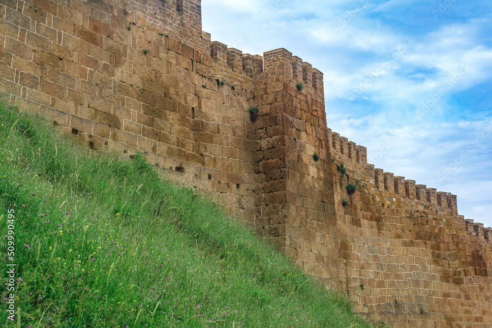 wall of a medieval fortress above a rampart overgrown with grass against the sky, Naryn-Kala citadel in Derbent