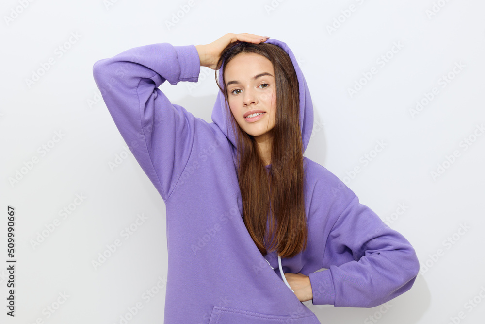 a gentle beautiful woman stands on a white background in a purple tracksuit put a hood on her head holding it with her hand, hiding the second one in the folds of a hoodie a gentle beautiful woman stands on a white background in a purple tracksuit put a hood on her head holding it with her hand, hiding the second one in the folds of a hoodie