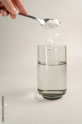 Woman pours collagen powder or protein in a glass of water on a beige background. A healthy and anti aging supplement. Copy space photo