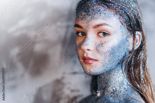 Young beautiful girl in fantastic creative makeup with rhinestone, dark background. Art beautiful girl model with cosmic make-up on face and body blue and silver skin color 