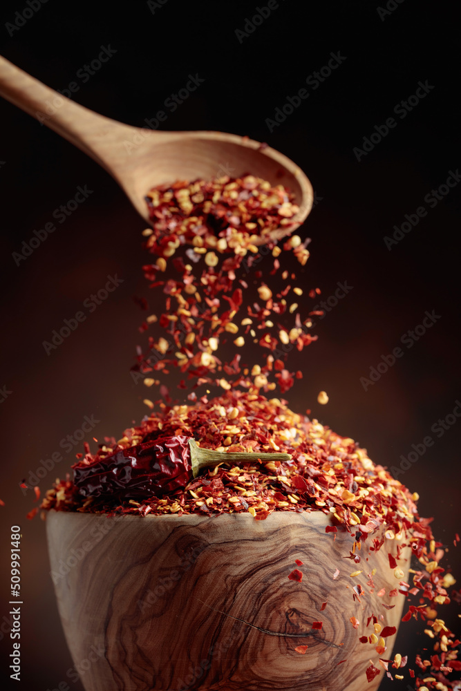 Chilli flakes are poured into a wooden dish.
