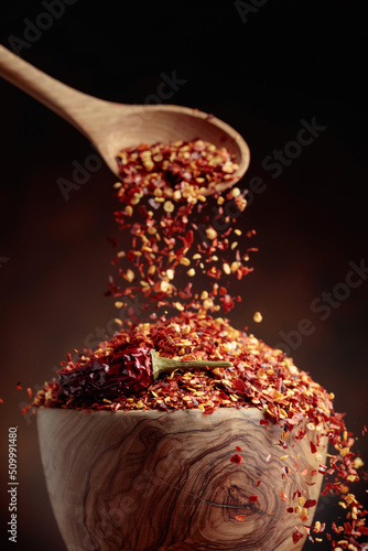 Chilli flakes are poured into a wooden dish.