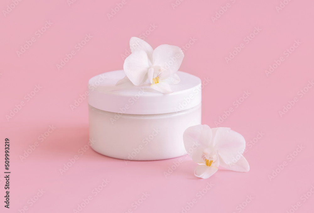White cream jar near white orchid flowers on light pink close up. Mockup. Skincare product White cream jar near white orchid flowers on light pink close up. Mockup. Skincare product
