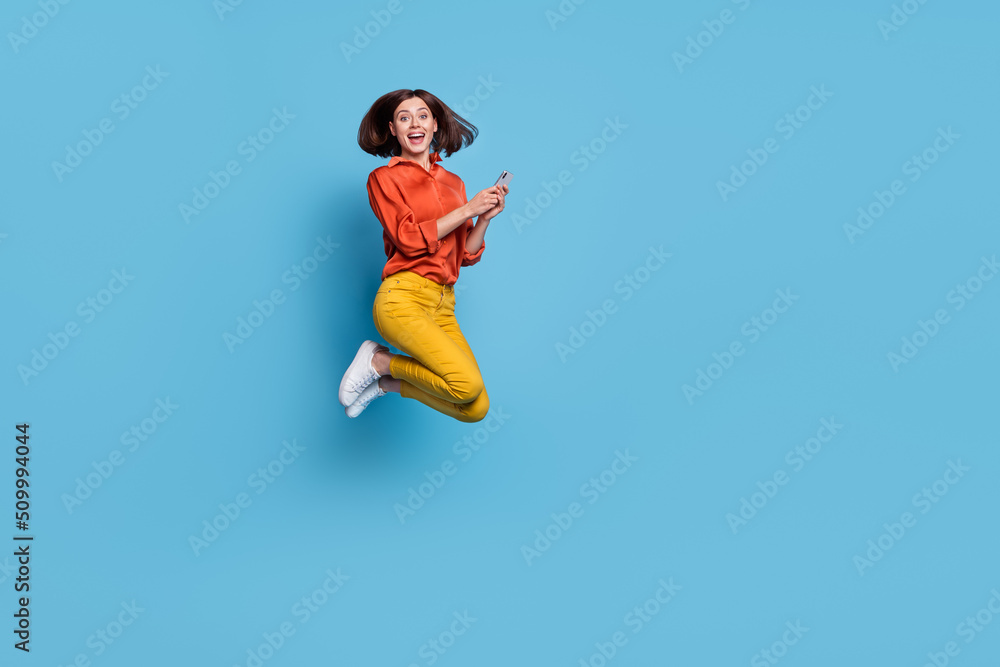 Full body profile side photo of young woman jump use mobile like repost fast connection isolated over blue color background Full body profile side photo of young woman jump use mobile like repost fast connection isolated over blue color background