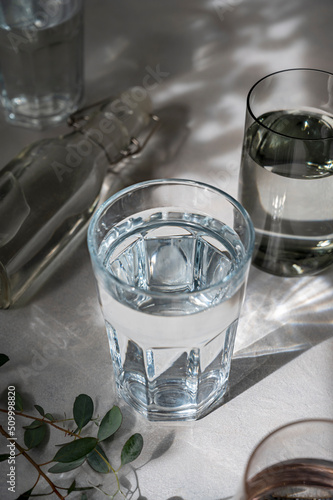 Glasses with water, abstract summer shadows on background. Drinking water concept, clean water