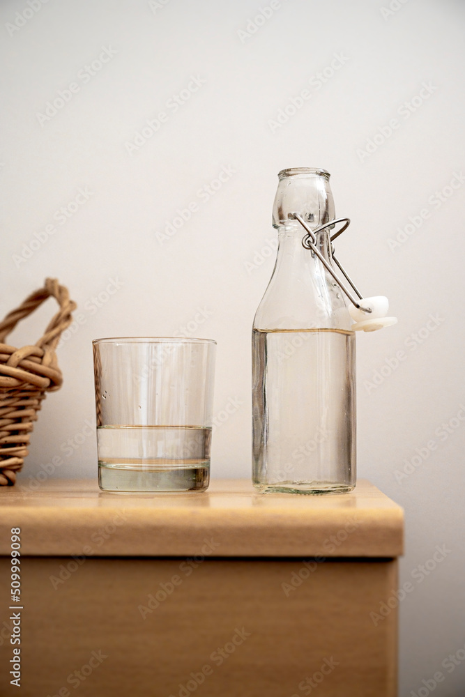 Glass bottle and a drinking glass with water on woodent table, indoor. Drinking water, healthy lifestyle. Glass bottle and a drinking glass with water on woodent table, indoor. Drinking water, healthy lifestyle.