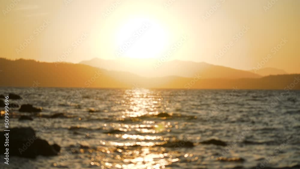 Defocused magic 4k slow motion video landscape of amazing peaceful sunny sunset over scenic sea. Dark silhouettes of mountains, orange sunset sky with sun circle, waves of sea water with reflections