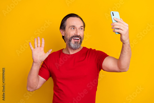 Photo of funky pretty retired man wear red t-shirt waving arm video call modern gadget isolated yellow color background