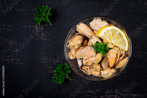 Delicious mussel meat with lemon and fresh parsley on a dark background. Top view, flat lay