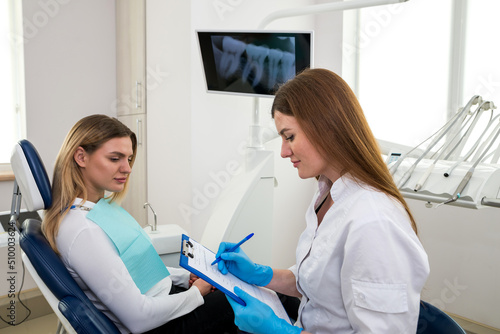 Dentist keeping medical history asking patient for information before treatment while sitting on a chair in a box