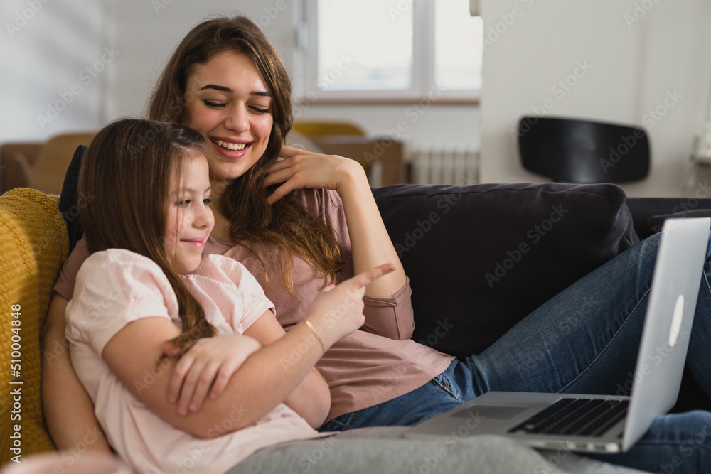 Obraz premium mother and daughter laying on sofa in living room and using laptop computer