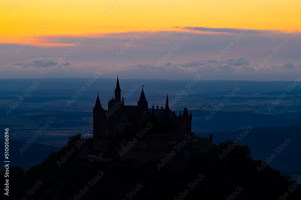 Historic castle silhouette on a hill in Germany near Hechingen south of Stuttgart at evening blue hour. Colorful twilight panorama with iconic monument seen from Zellerhorn viewpoint.