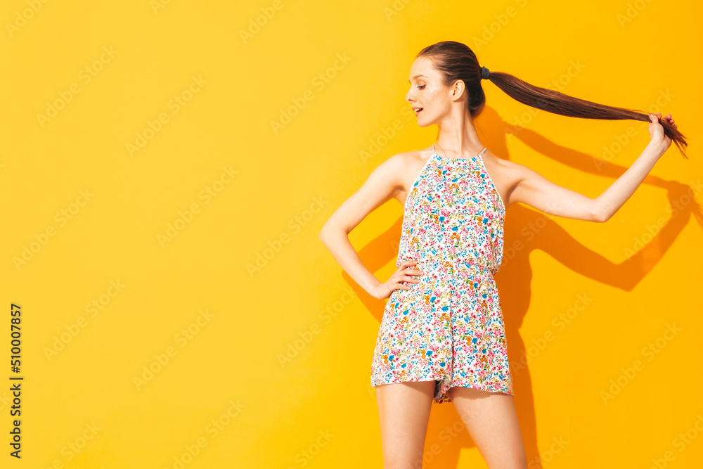 Young beautiful smiling female in trendy summer overalls. Sexy woman with posing near yellow wall in studio. Positive model having fun. Cheerful and happy. Holding tail in hands Young beautiful smiling female in trendy summer overalls. Sexy woman with posing near yellow wall in studio. Positive model having fun. Cheerful and happy. Holding tail in hands