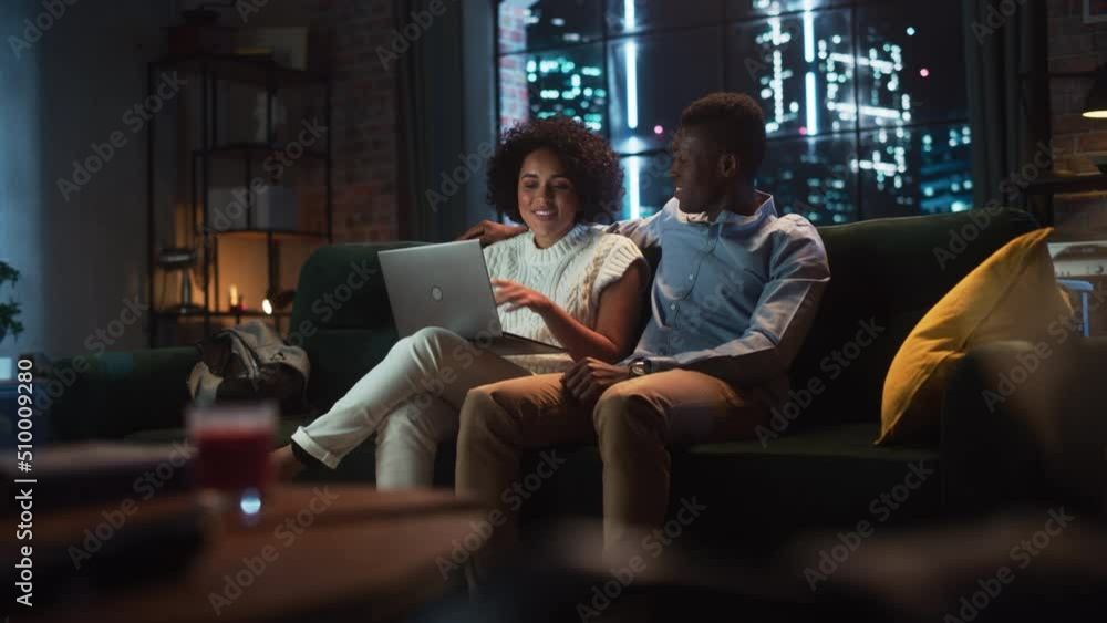 Young Black Couple Use Laptop Computer, while Sitting on a Couch in Cozy Stylish Apartment. Boyfriend and Girlfriend do Online Shopping, Use Social Media, Watch Funny Videos, Streaming Service Young Black Couple Use Laptop Computer, while Sitting on a Couch in Cozy Stylish Apartment. Boyfriend and Girlfriend do Online Shopping, Use Social Media, Watch Funny Videos, Streaming Service