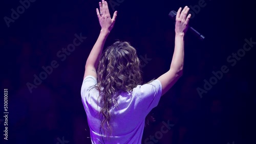 Woman on stage with a microphone worshiping with raised hands at a church. photo