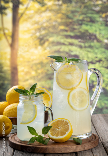 Glass and pitcher of lemonade with summer background