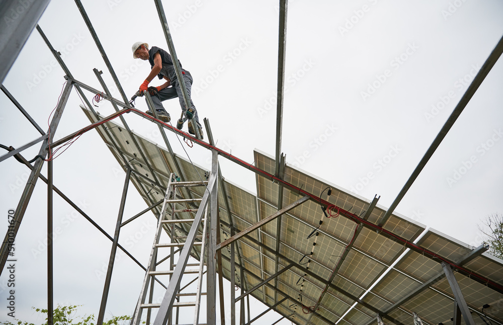 Man engineer standing on metal rail and using electric drill while installing support structure for photovoltaic solar panels. Isolated on white background.