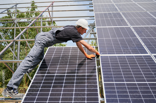 Man engineer solar installer placing solar module on metal rails. Male worker installing photovoltaic solar panel system. Concept of alternative energy and power sustainable resources.
