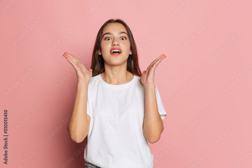 Portrait of young charming girl in white t-shirt marvels isolated on pink background. Concept of beauty, art, fashion, youth and emotions Portrait of young charming girl in white t-shirt marvels isolated on pink background. Concept of beauty, art, fashion, youth and emotions
