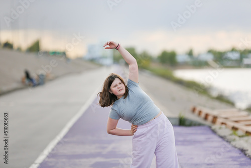 Overweight European teenager kid girl in tracksuit warms up, does sports exercises on concrete embankment, Sports and teenagers, overweight teenagers,