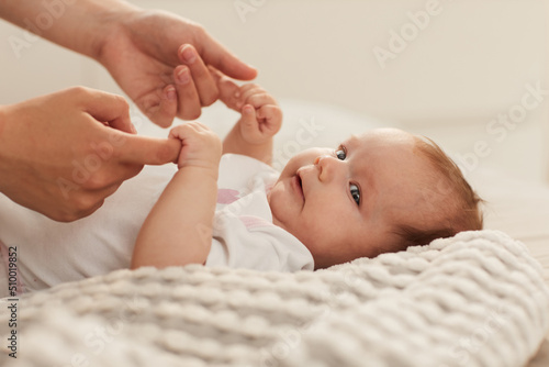 Adorable little baby holding fingers of mother when lying on soft blanket bed