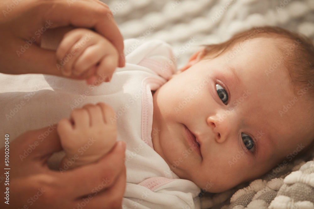 Face of cute little baby girl with beautiful big grey eyes lying on bed in white bodysuit
