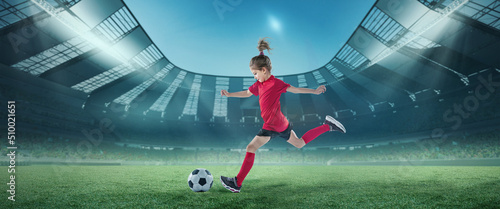Portrait of little girl  football player in red uniform in motion  hitting ball at the open air stadium. Championship