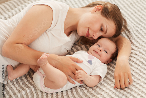 Smiling beautiful young woman lying on bed and playing with her cute happy baby