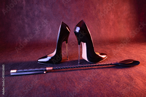 Konstfotografi Black shiny high heel shoes and a whip on a dark background