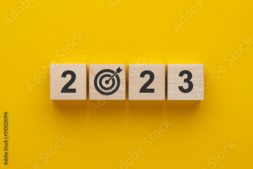 Goal in the new year 2023. Wooden cubes with numbers 2023 and target icon on yellow background. Business development strategy, advancement and goal concept.