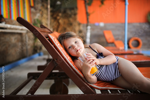Fotografia, Obraz Cute child girl in wide-brimmed hat and sunglasses in swimsuit on wooden sun lou
