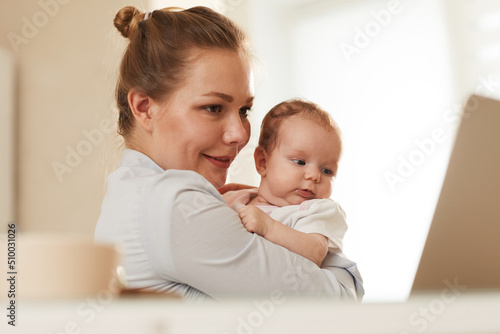 Young smiling mother showing her baby to grandmother who is calling them through Skype