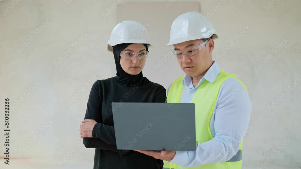Portrait of successful real estate arabian muslim investor and chinese engineer standing indoors in empty building wearing safety helmet and formal suit. International business. Buying apartment. Portrait of successful real estate arabian muslim investor and chinese engineer standing indoors in empty building wearing safety helmet and formal suit. International business. Buying apartment.