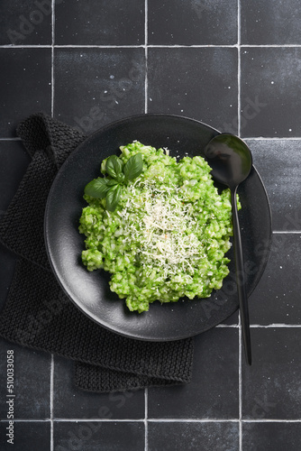 Italian risotto. Delicious risotto with pesto sauce or wild garlic pesto, basil, parmesan cheese and glass of white wine on old black tiles table background. Italian dinner. Top view with copy space.