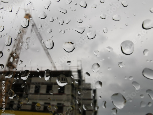 Regentropfen auf einer Scheibe mit Blick auf eine Baustelle symbolisch für verregnete Baubranche