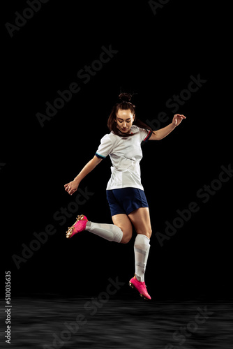 Young caucasian sportive woman, female soccer, football player in motion isolated on dark background. Sport, action, competitions, games and fitness concept