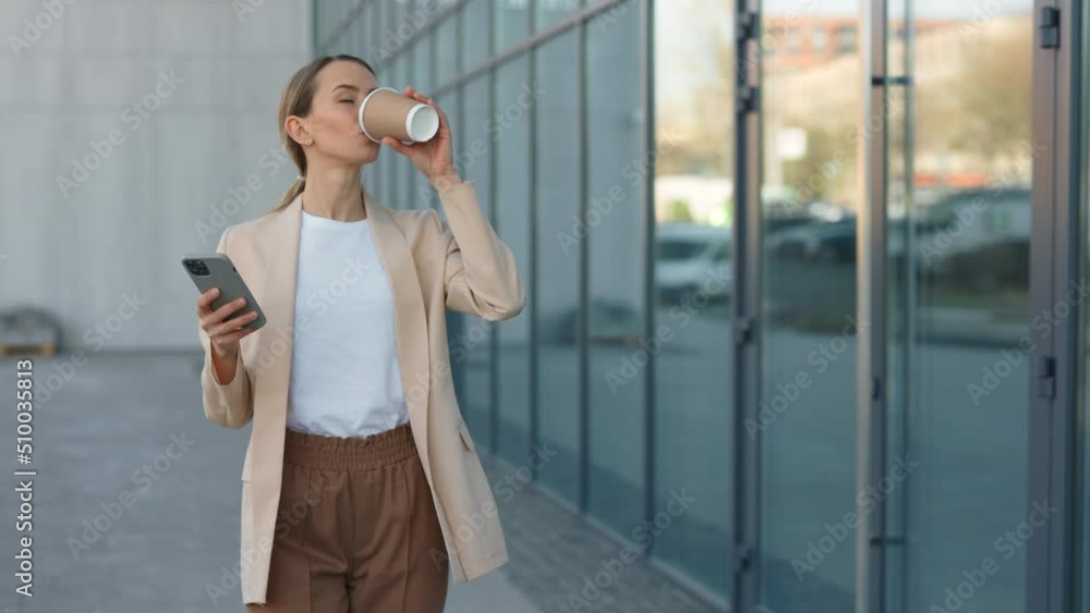 Charming blond woman in formal wear using modern smartphone while walking outdoors and drinking coffee-to-go. Business, lifestyles and coffee break concept. Charming blond woman in formal wear using modern smartphone while walking outdoors and drinking coffee-to-go. Business, lifestyles and coffee break concept.