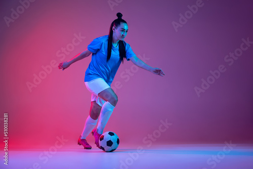 Dribbling. One sportive girl  female soccer player training with football ball isolated on purple studio background in neon light. Sport  action  motion  fitness