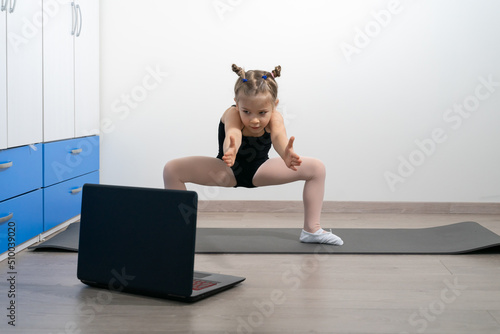 kid girl in a gymnastic leotard is engaged in classical dances with a trainer online. Self-isolation during quarantine.