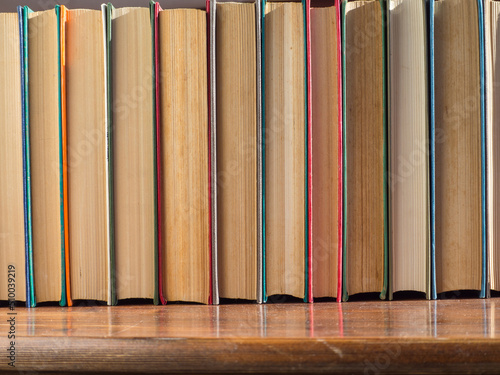 A row  of old hardcover books. Books on a wooden shelf, turned back cover. Books from the Home Library
