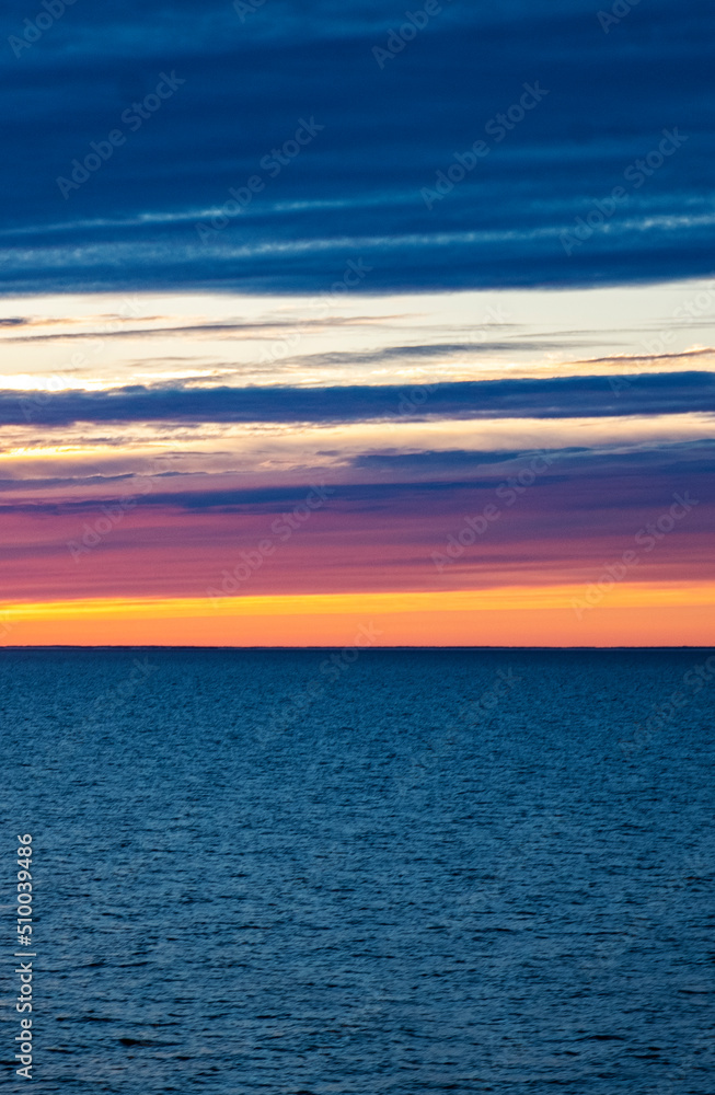 Bright orange sunset over the sea, streaks of sunlight across the sky. vertical photo