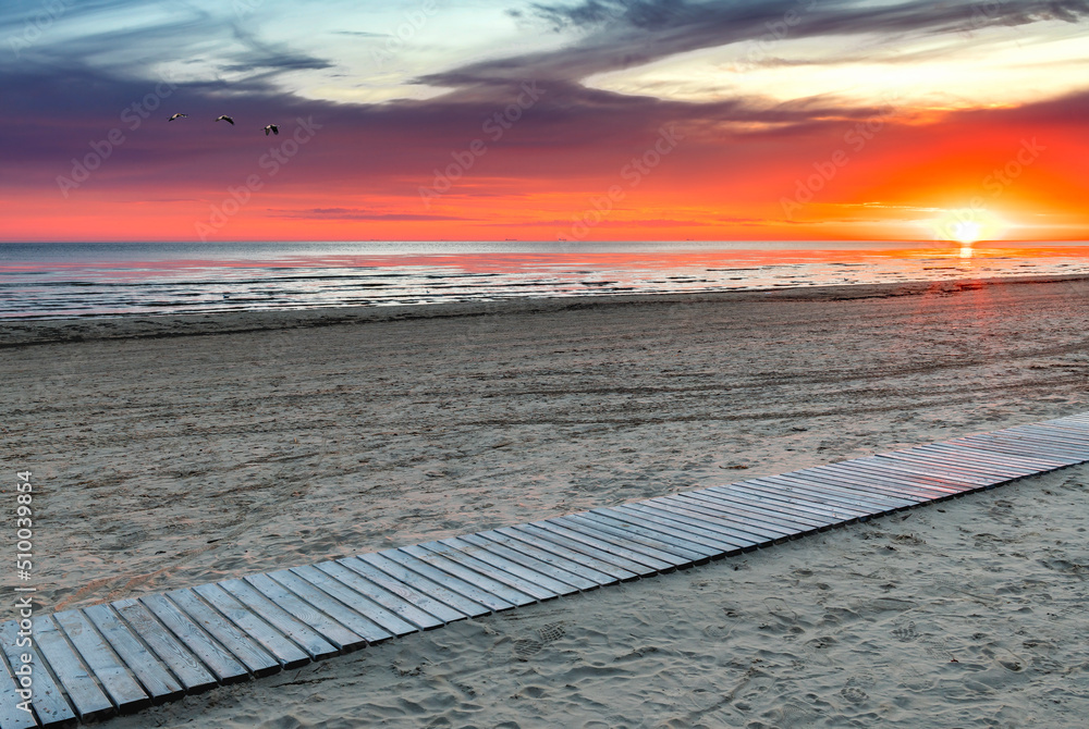Colorful sunset on the beach of the Baltic Sea with wooden footpath