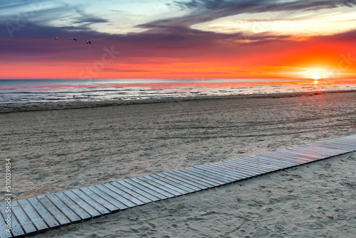 Colorful sunset on the beach of the Baltic Sea with wooden footpath