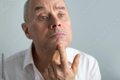 close-up charismatic mature man 60 years old applies aftershave on the face, critically examines face, skin, wrinkles, upset because age-related changes, midlife crisis, hair loss, selective focus