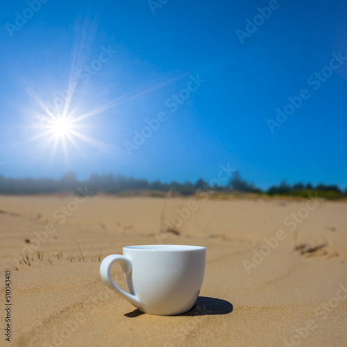 closeup white coffee cup on sand at hot summer sunny day