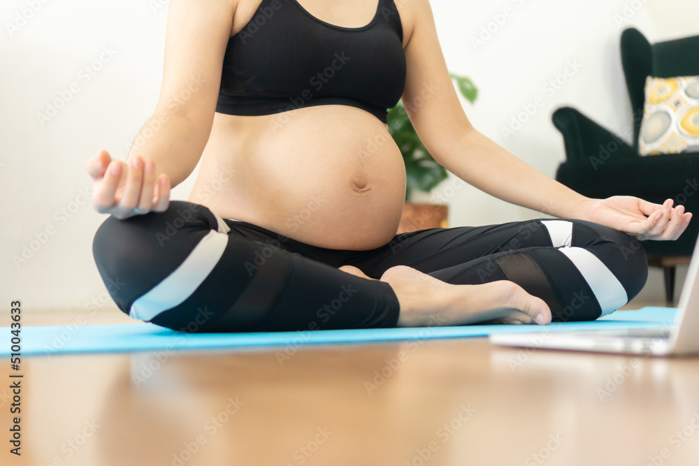 Asian pregnant woman doing yoga and meditating indoors at home, lotus position Asian pregnant woman doing yoga and meditating indoors at home, lotus position