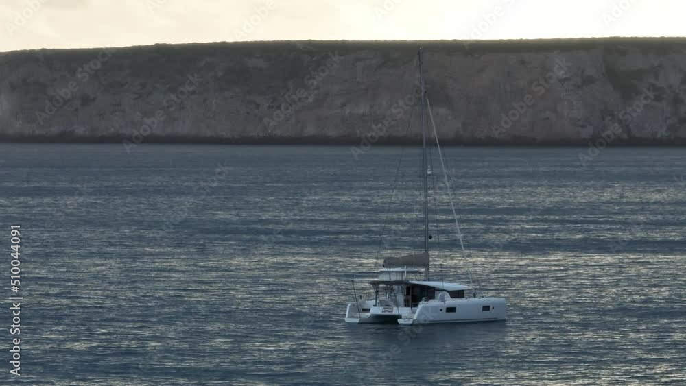 Beautiful aerial shot of a catamaran anchored in front of a coastline with cliffs at sunset Beautiful aerial shot of a catamaran anchored in front of a coastline with cliffs at sunset
