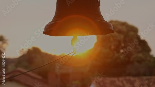 Close up shot of hanging bell in the church of the Missoes Jesuitas Bolivia with sunset in the background.Close-up view of metal orthodox church bells. Bottom view of the Church bells
 photo