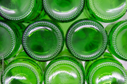 Bottoms of empty green glass bottles on white background, top view.
Green soda, wine glass bottle texture for copy space.
Recycling of environmental green glass waste. Recycling  concept.