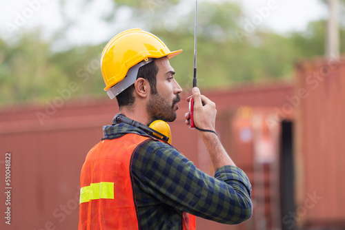 Industrial engineer in hard hat containers box background, Dock worker man talks on two-way radio at containers cargo, Logistic and transportation concepts